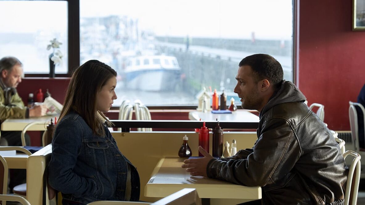 A man in his 30s at a diner table talking to a teenage girl